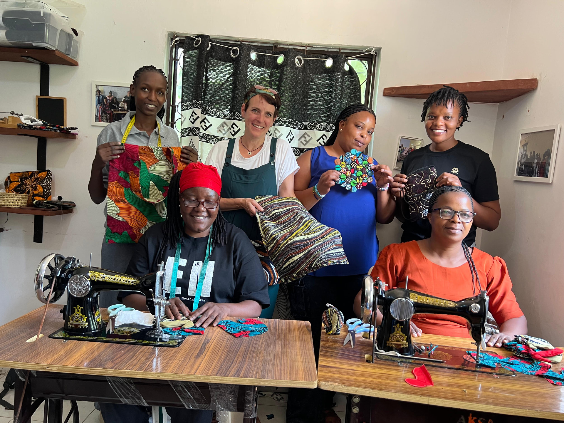Frauen des Nähprojekts zeigen ihre selbst genähten Taschen an den Nähmaschinen